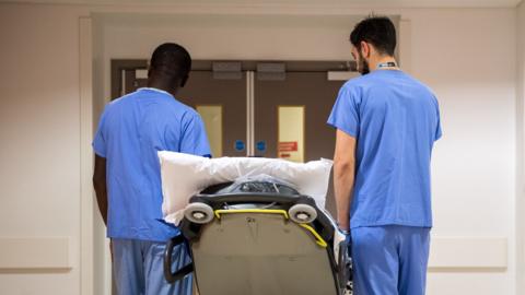 Medical staff accompany a patient on a trolley through a corridor inside the Royal London Hospital, part of the Barts Health NHS Trust, in London, U.K., on Thursday, Jan. 11, 2018. 