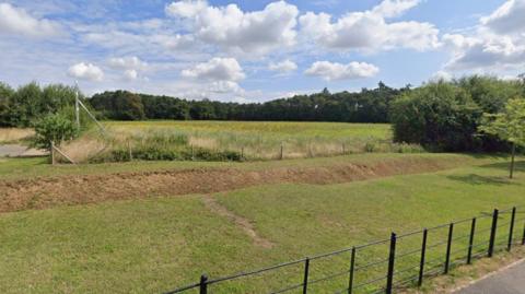 A large field with a muddy dip and black waist level fence.