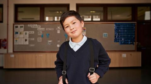 Smiling school boy standing in the doorway of a school. 