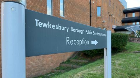 Sign pointing to the entrance of a red brick building (Tewkesbury Borough Council), reads Tewkesbury Borough Public Services Centre. Then the line below reads 'reception'.