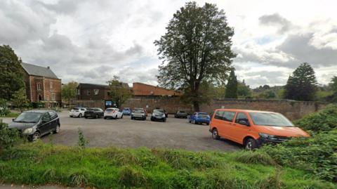 A picture of the North Car Park near Bristol Zoo Gardens in Clifton with cars visible in the parking spaces and a grass verge