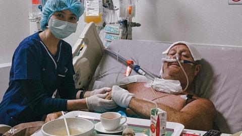 Lee Francis in hospital in Thailand with a nurse helping him with physio