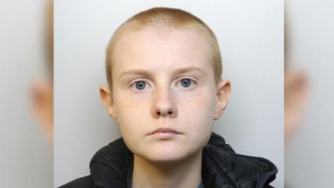 Alina Burns is a young woman with a shaved head. The image is a police mugshot. 