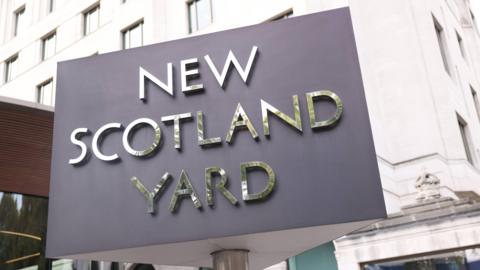 The revolving sign outside New Scotland Yard. A stone-clad building is in the background.