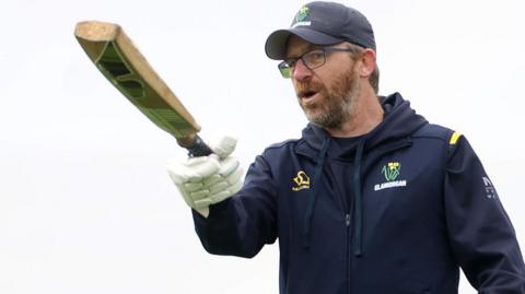 Richard Dawson gives instructions to his players while pointing with a bat