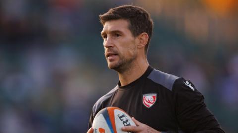 Gloucester defence coach Dom Waldouck holding a ball on the pitch before Gloucester's Prem match with Bath