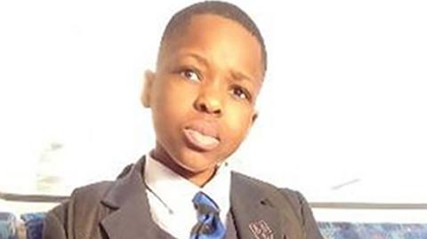 Schoolboy Daniel Anjorin sitting in a dark school uniform on a Tube. He has a blue and black tie and straps of his rucksack can be seen on his shoulders
