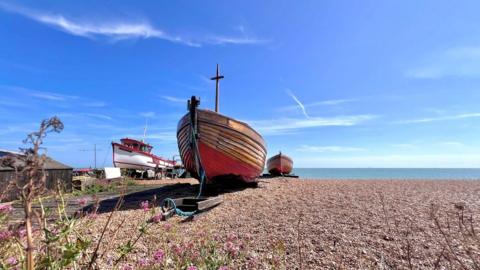 Three boats on a pebble beach in front of the sea.