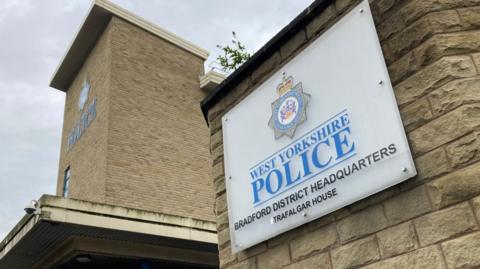 White sign on a pale stone wall with the words West Yorkshire Police Bradford headquarters written on it in black