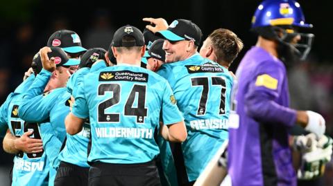 Brisbane Heat players celebrate their win while a Hobart Hurricanes batter walks off the ground