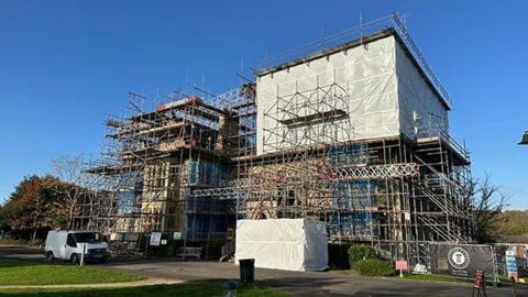 A building covered in scaffolding. There are clear blue skies above.