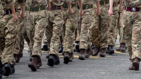 Close up shot of the legs of British soldiers who are in uniform and marching through the street