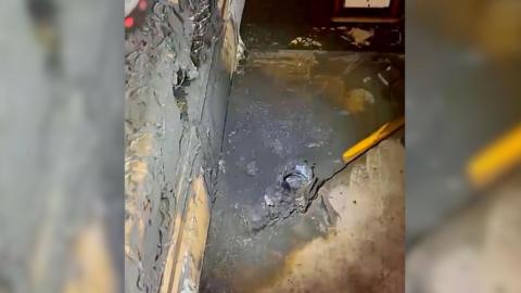 A bed and carpet are burnt and covered in soot, a vacuum cleaner is on the floor with a hole burnt through the battery