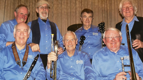 The seven-strong Merseysippi jazz band are wearing pale blue shirts, and holding their instruments as they sit or stand.