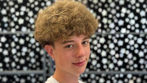Mathieu is smiling into the camera, he is 15 and has brown curly hair.
