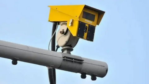 A mounted yellow CCTV camera against a blue sky background