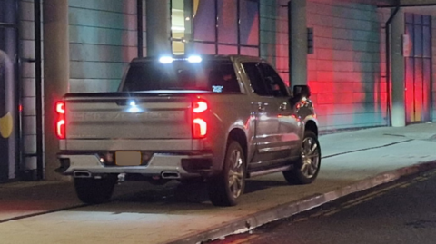A grey pickup truck parked on a pavement. 