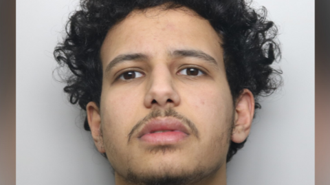 Police custody image of a man with dark curly hair and thin beard.