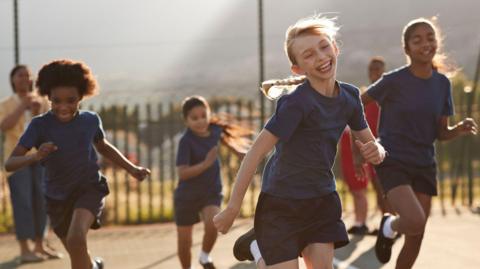A group of primary school children running and smiling in PE kit