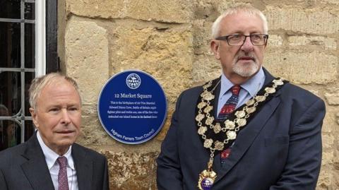 Two men pose by a blue plaque. One is wearing mayoral chains.