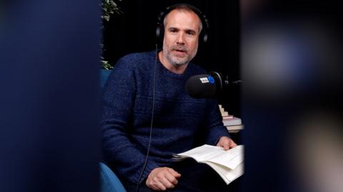 Dr Xand van Tulleken sits wearing headphones and a dark blue top