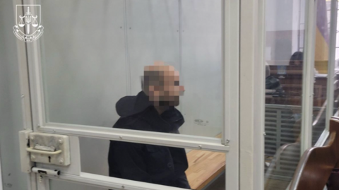 A man sits behind glass in the dock in court, his face pixelated.