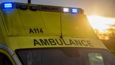 A stock photo of an ambulance with blue lights flashing.