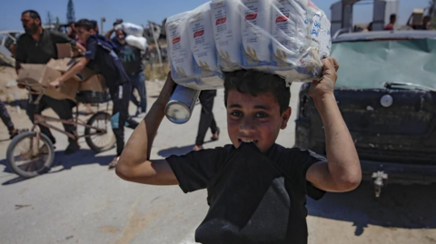 A child carries supplies on his head while walking from a GHF distribution centre in central Gaza.
