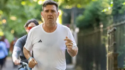 Burnham, wearing a white T-shirt with an Adidas logo, runs in a park