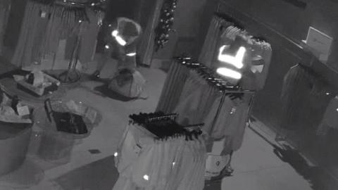 A screengrab from a CCTV camera. There are two men dressed in high visibility jackets stuffing clothes into bags.