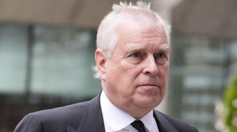 Andrew Mountbatten Windsor has grey hair. He is looking to the right. You can see the top of a suit and black tie.