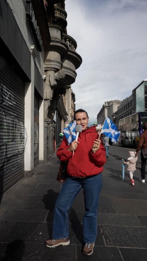 Harriet Fisher standing in the street holding mini Scotland flags and a microphone