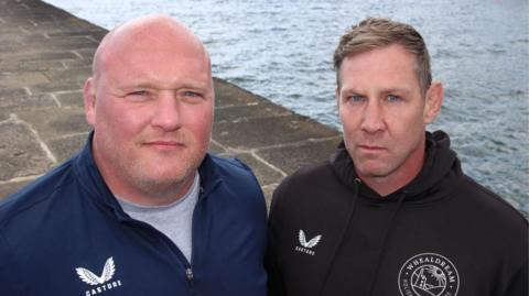 Two men one in blue tracksuit and one in black tracksuit 