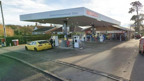 View of the Gill Marsh Forecourts petrol station in Bilsby in Lincolnshire it has a white canopy covering the fuel pumps and a redbrick shop at the back