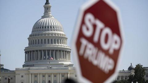 File image of the US Capitol building with a blurry sign in the foreground that reads "Stop Trump"