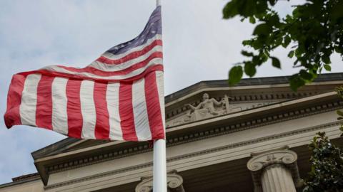 Outside shot of the main entrance of a court . A US flag flies in front of it from a white pole. At the top of the temple-like building, in the tympanum, is a stone statue of a woman holding a sword in her left hand