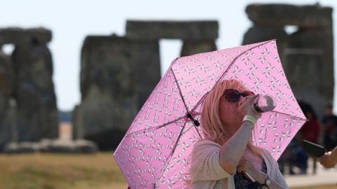 Woman with pink umbrella drinks water