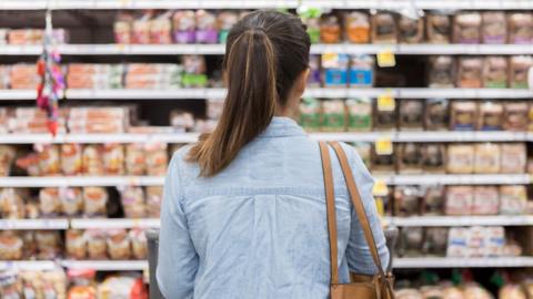 A person stands in front of a shop shelf looking at a wide variety of products