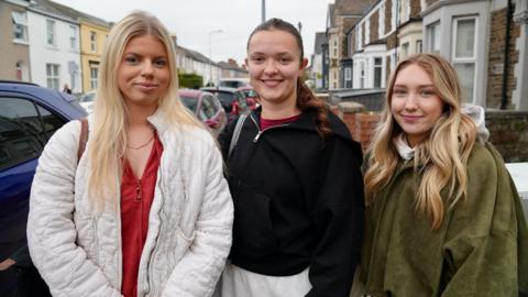 Three students are standing next to each other looking at the camera.