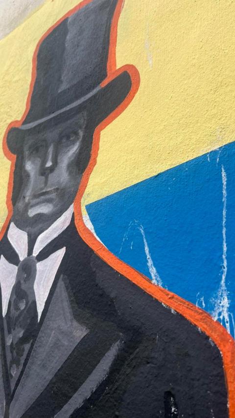 A painting of a man in a suit and top hat on the side of a wall.