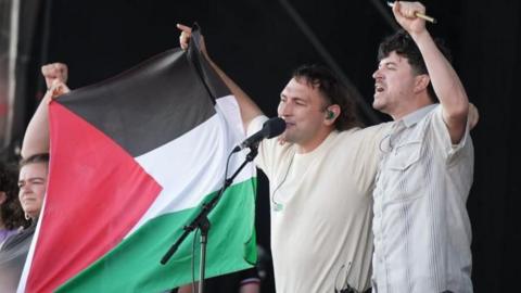 Two men and a woman on stage with a Palestinian flag between them