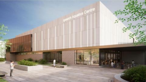 Artist's impression of the new aquatics centre in Ipswich. It is a large, rectangular building that is grey with white vertical lines on its top half. Its entrance has tall galss windows. Outside the building are benches and greenery.