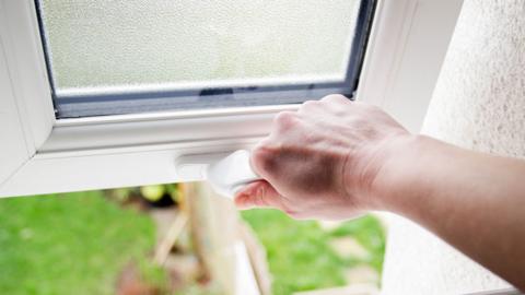 A hand opening a window of a house.