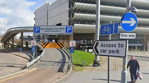 Road ramp entrance to Preston Bus Station with signs and pedestrian walking nearby.