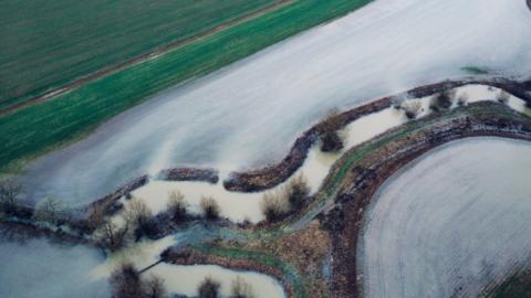 A brown river has burst its banks onto nearby fields.