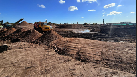 A yellow digger moves around mounds of earth on the former Rolls Royce factory site