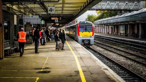 A train arrives at Shrewsbury Station, as passengers wait to board. There are signs above indicating they are standing on platform 4b.