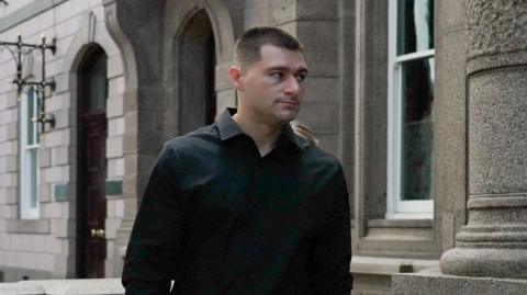A man wearing a black shirt walking into the royal court.