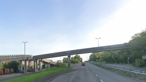 Footbridge over the road with car on it on a clear blue day.