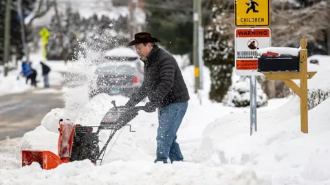 A man uses a small snow plough on a large pile of snow on a residential street in Connecticut.